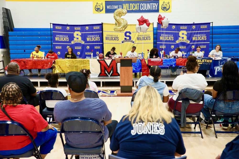 9 student athletes sit at tables to sign their college letters of intent