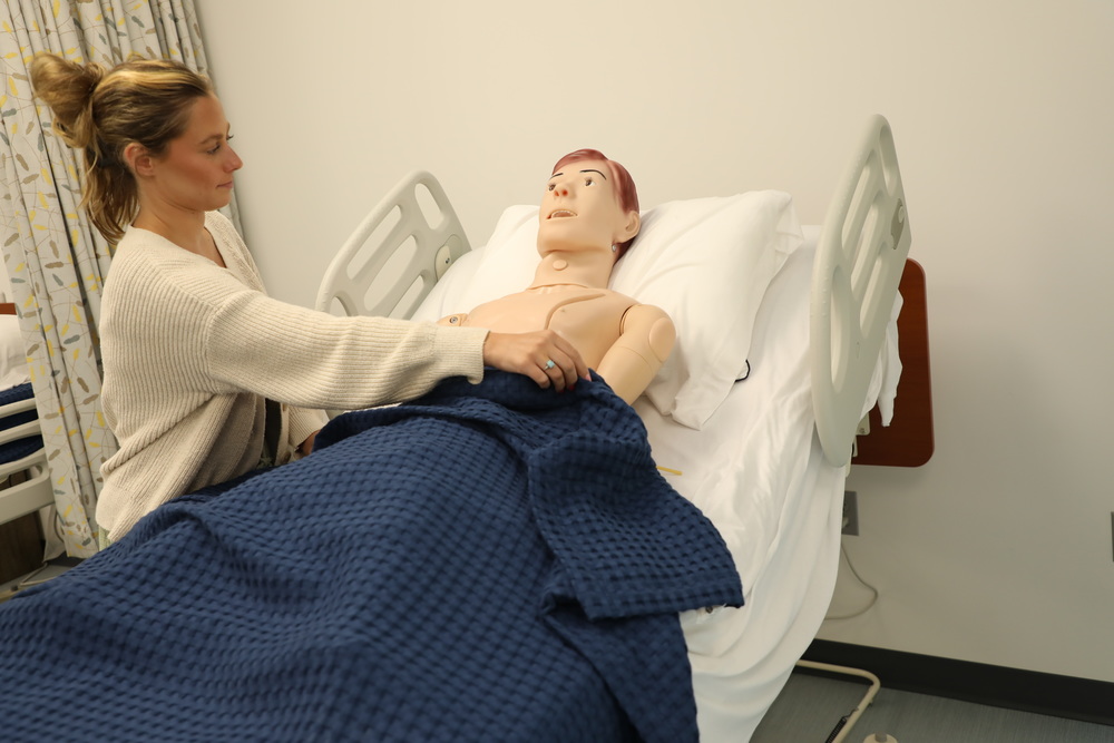 A woman tucks in a medical dummy in the new STNA room