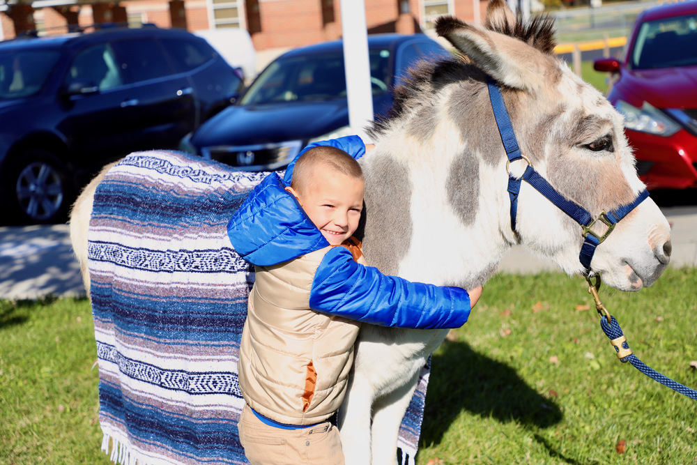 A first grade student hugs a donkey that illustrates as a 'biblioburro'