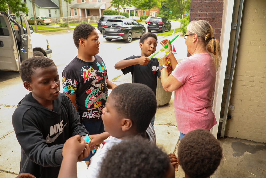 Woman handing out popsicle to kids.