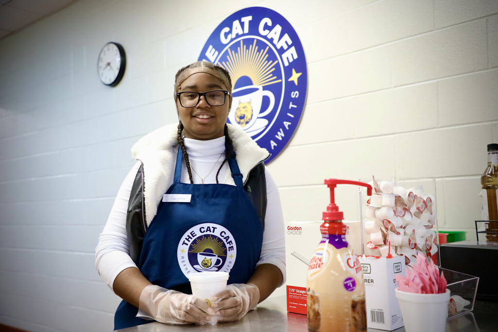 A cat cafe student employee poses with a cup of coffee