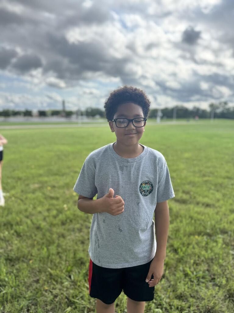 Student standing in a grass field giving a thumbs up