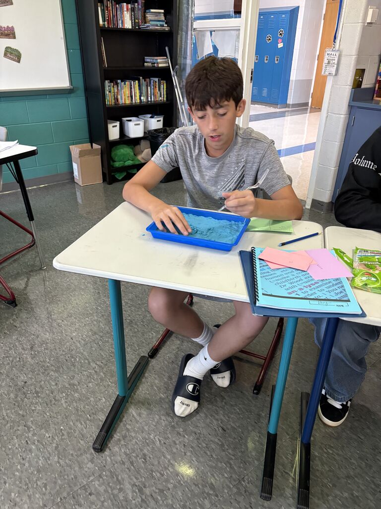 Students use kinetic sand and colored index cards to practice building complicated words with morphemes. 