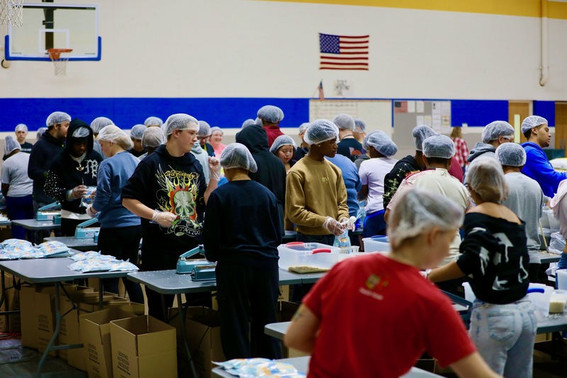 Students at several tables pack meals