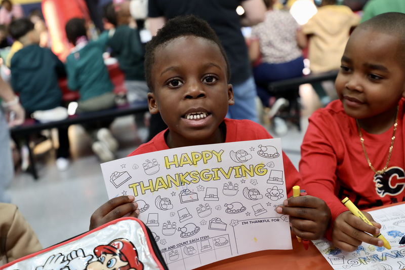 A male student holds up his coloring page placemat that says 'Happy Thanksgiving'