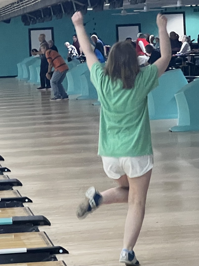 A young person celebrates a bowling score with arms raised at a bowling alley.