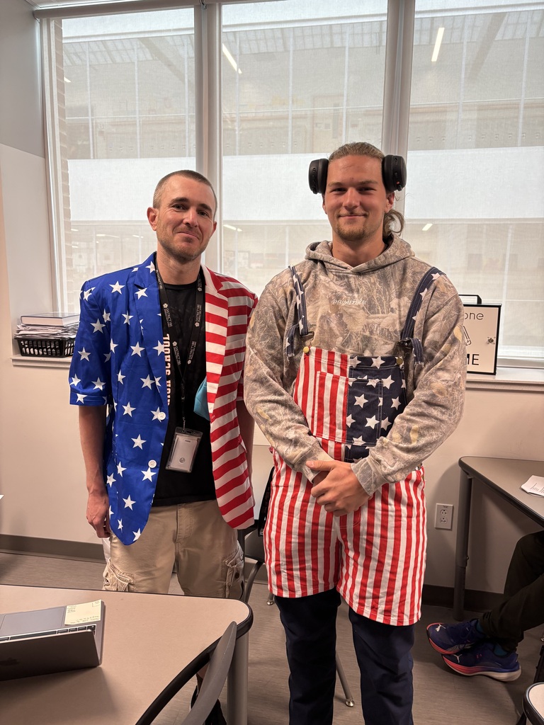 Two men in a room, one in an American flag jacket and the other in a patriotic apron.