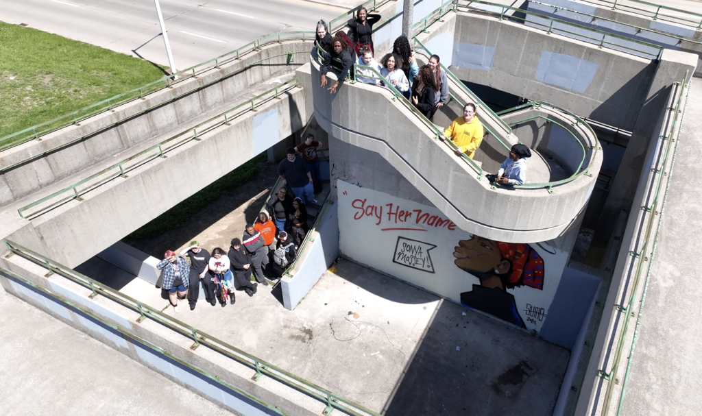 A group of people stands on the steps of a bridge, some on the stairs, with graffiti on the wall.