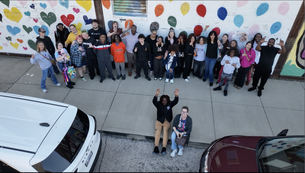 Group of people pose for photo in front of building with colorful, heart-shaped mural.