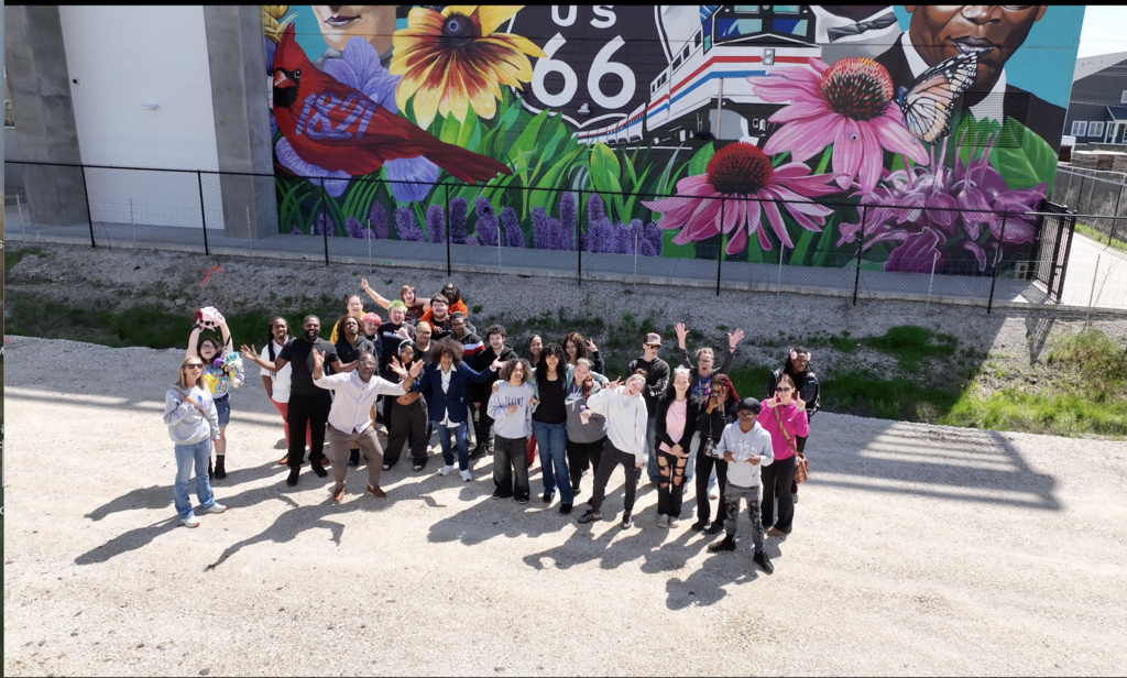 Group of people standing together in front of a mural with flowers, a bird, and number 66.