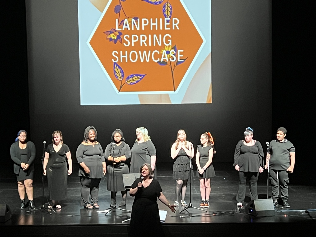 A group of singers on stage, one person speaking into a microphone. A screen behind them displays "Lanphier Spring Showcase."
