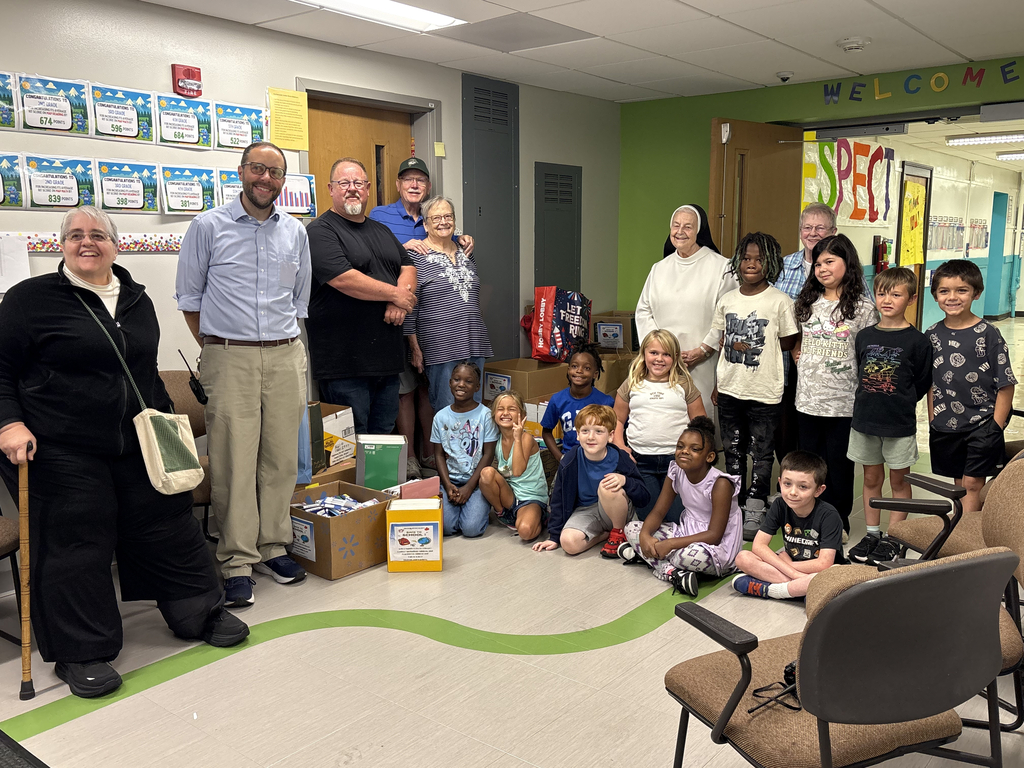 Several adults and children stand and crouch in a classroom. Adults pose for a photo while children smile.
