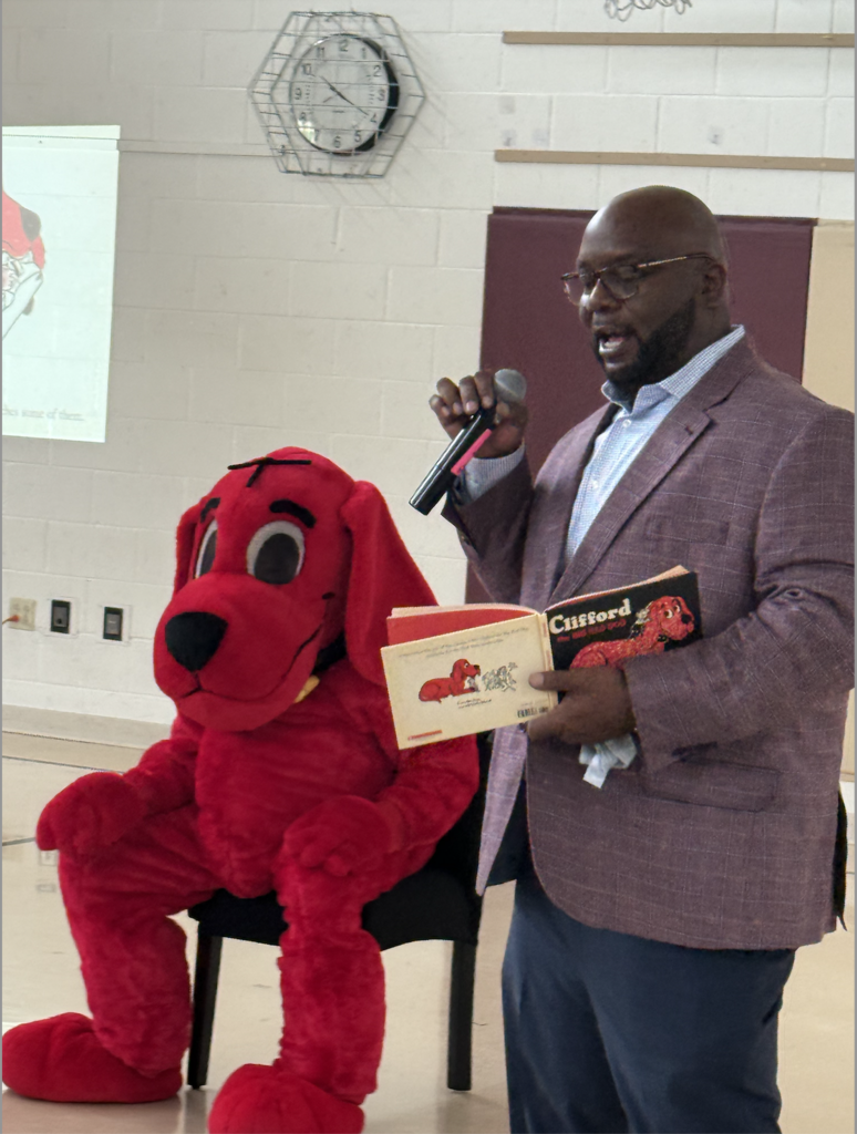 Superintendent Dr. Jordan reading Clifford the Big Red Dog book standing next to Clifford.