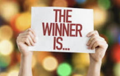Two hands holding a white sign with red text that reads "The winner is..." against a colorful, blurry background.