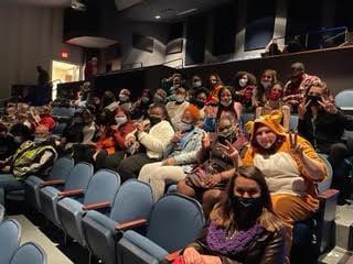 choir students on a field trip sitting in a dimly lit auditorium 