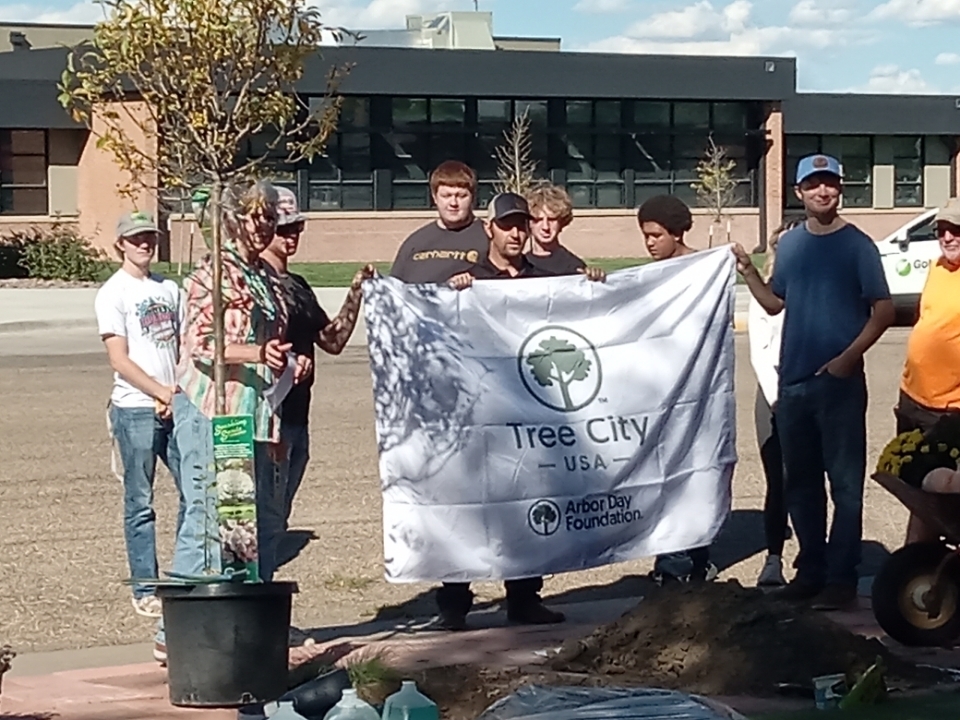 Interim Mayor, Josh Wittler, accepts Tree city USA flag from Tree Board members Kathy Self and Larry Duncan.