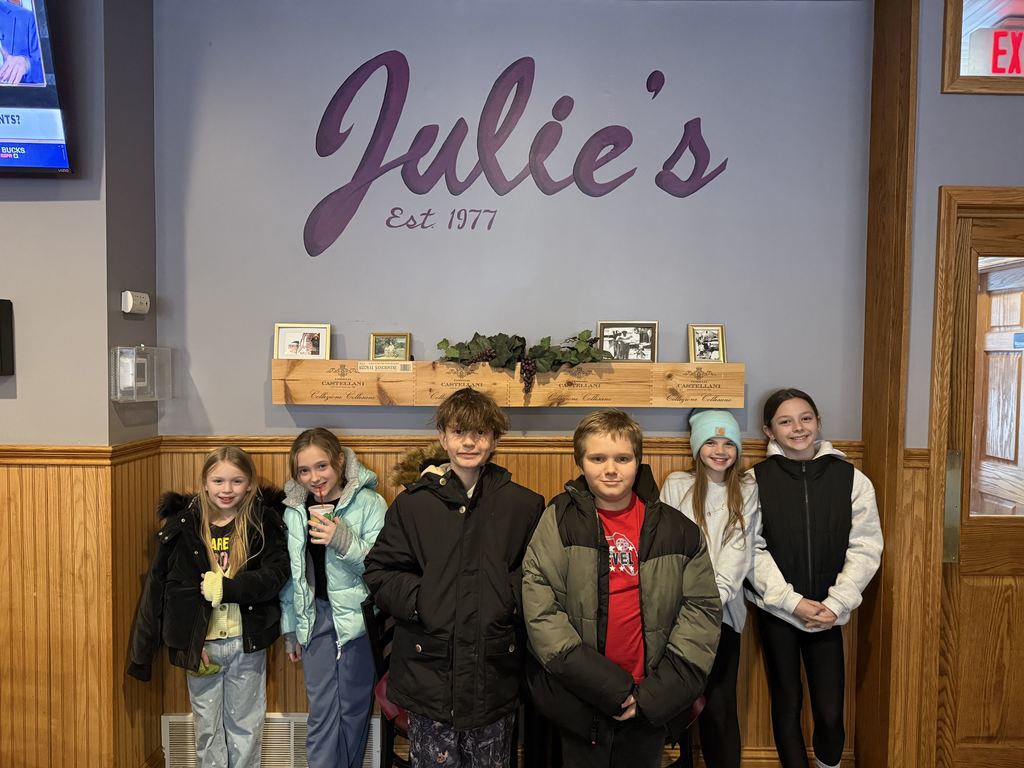 students pose for a photo in front of the Julie's sign. 