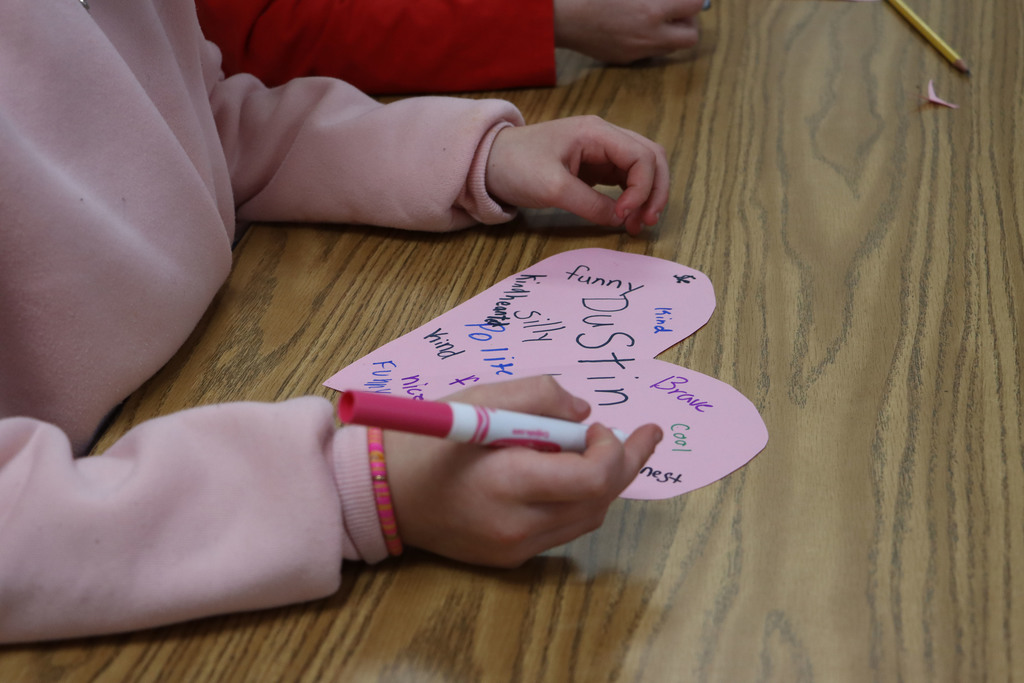 a student writes a character trait on a pink heart. 