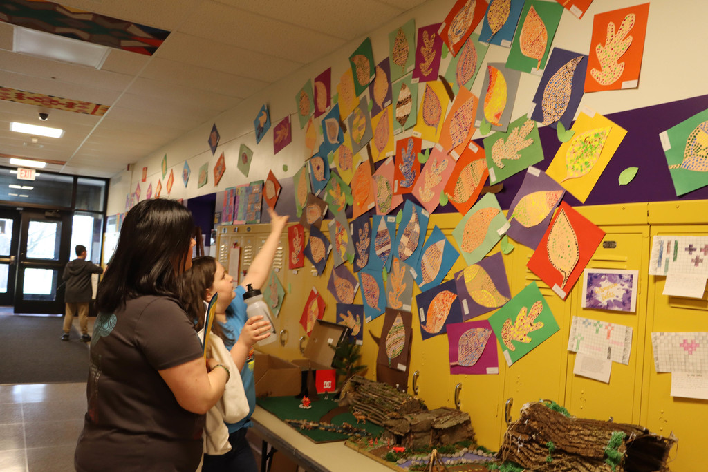 A student points out her artwork to her mom. 