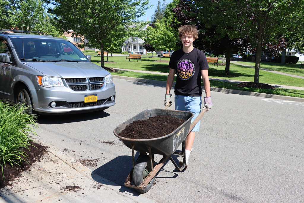 A senior pushes a wheelbarrow of dirt. 