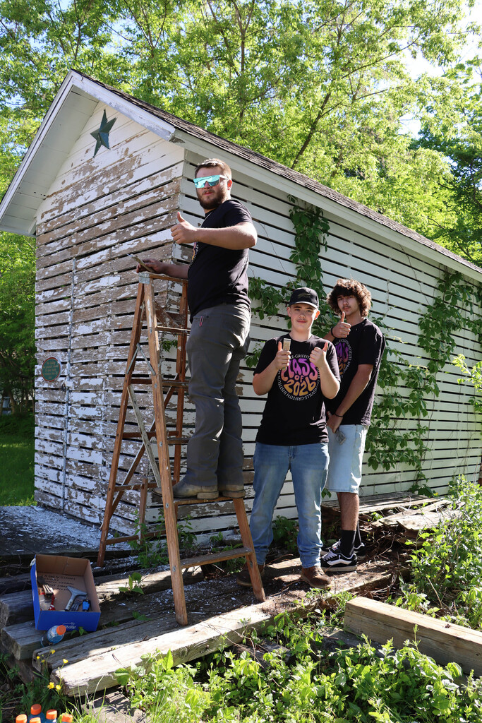 Three seniors remove paint from a building. 