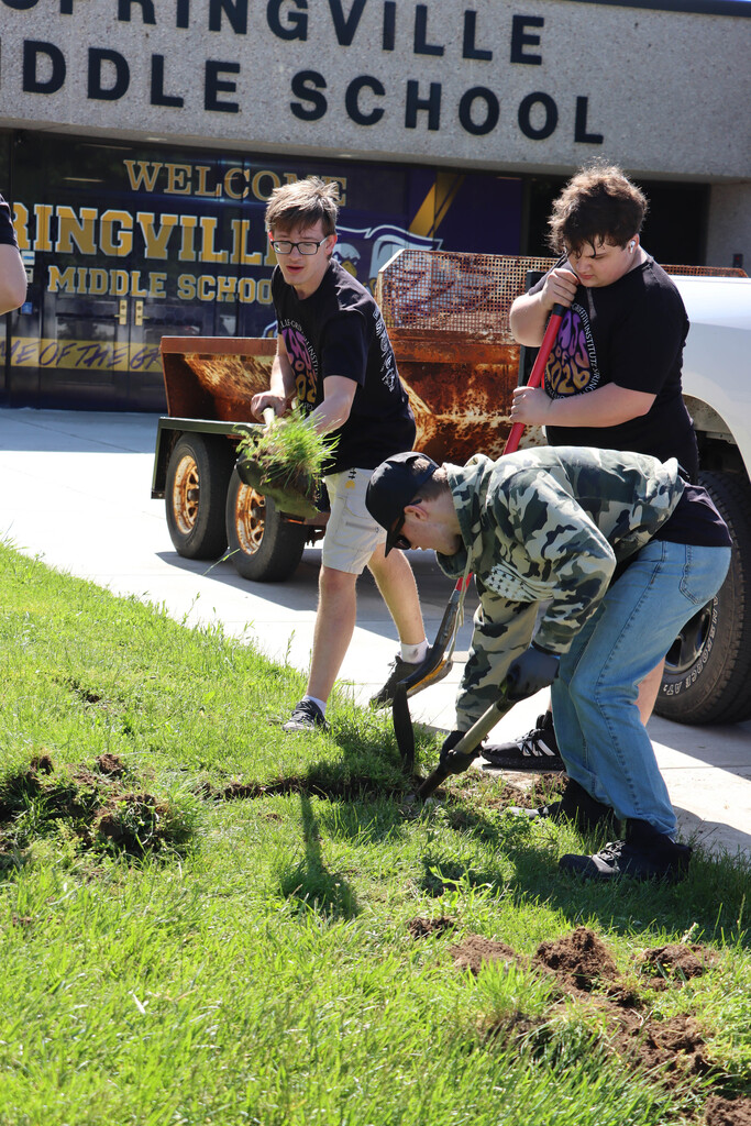 Three seniors dig grass for a garden at the middle school. 