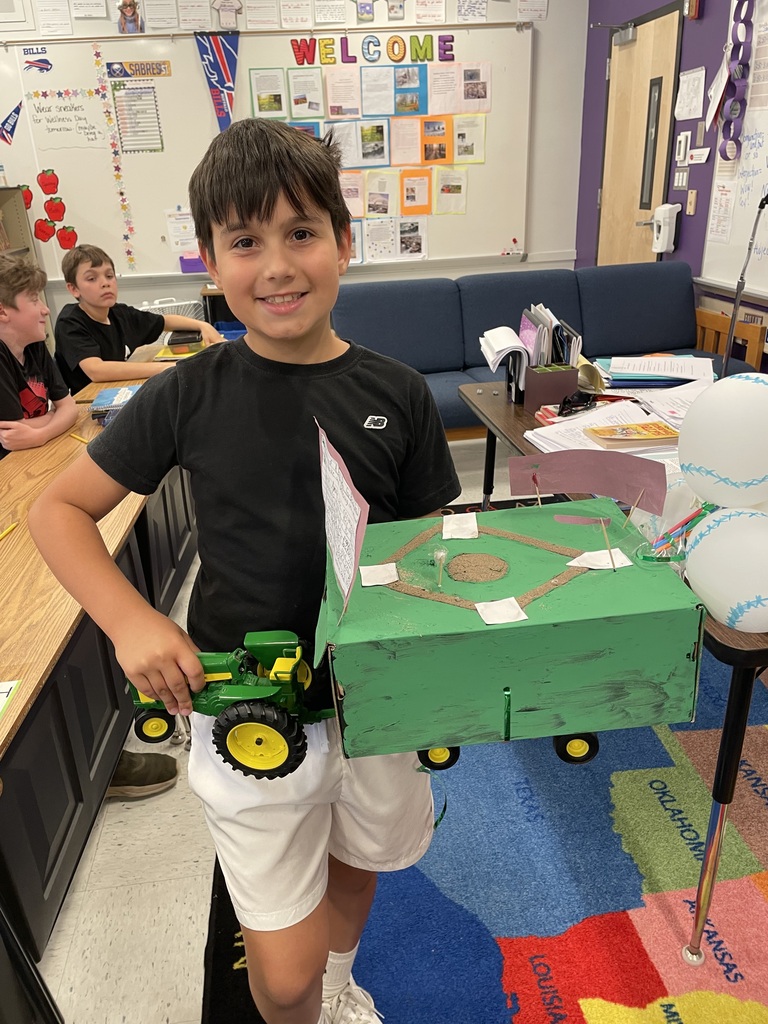 A student holds a float in the shape of a baseball field pulled by a tractor.