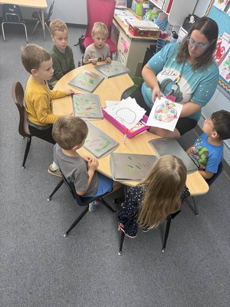 we are coloring on cookie sheets, then using spray bottles to spray where we colored. Then we laid our apple outline on top pulled it off to see the magic color transfer.