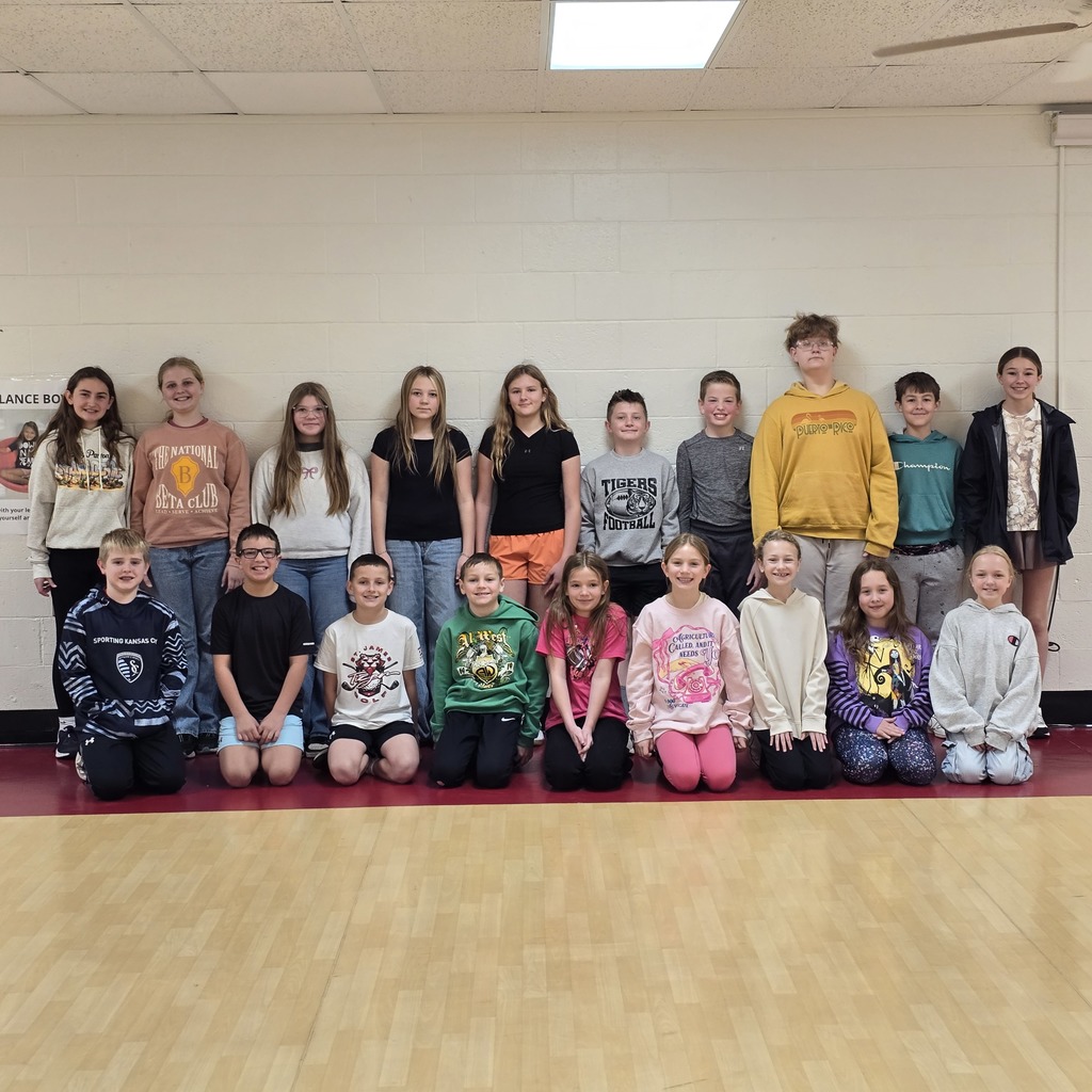 Group of students, standing and kneeling, posing for a photo in a room with a white wall.