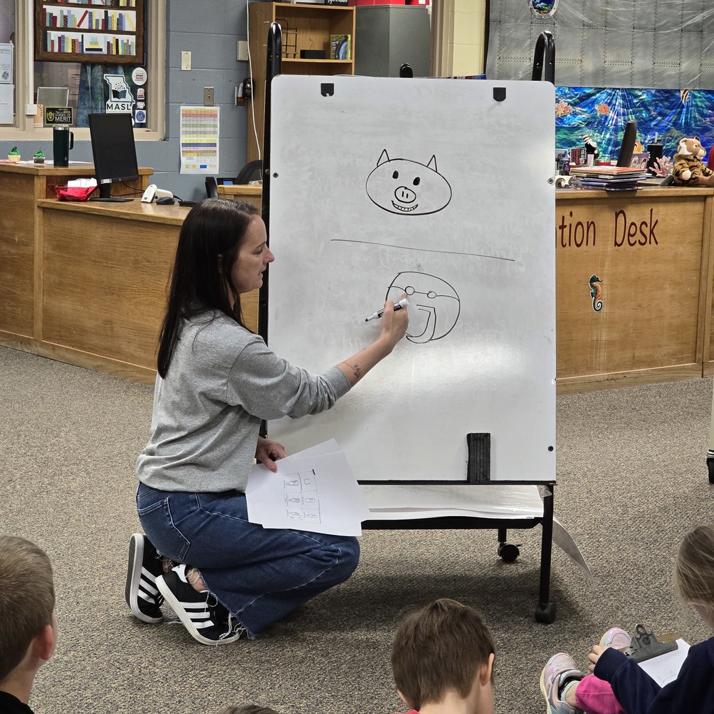 Woman drawing a pig on a whiteboard. Students sitting on the floor watching. Bright room with bookshelves and desk.