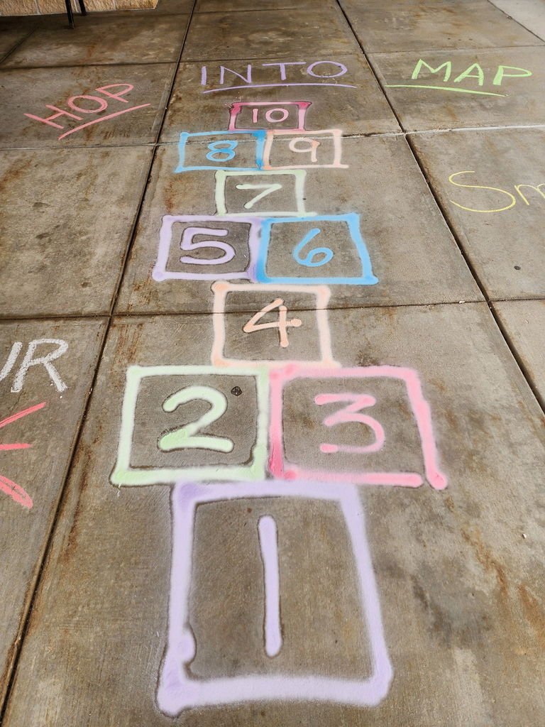 A hopscotch game drawn in multicolored chalk on a concrete surface, numbered from 1 to 10.
