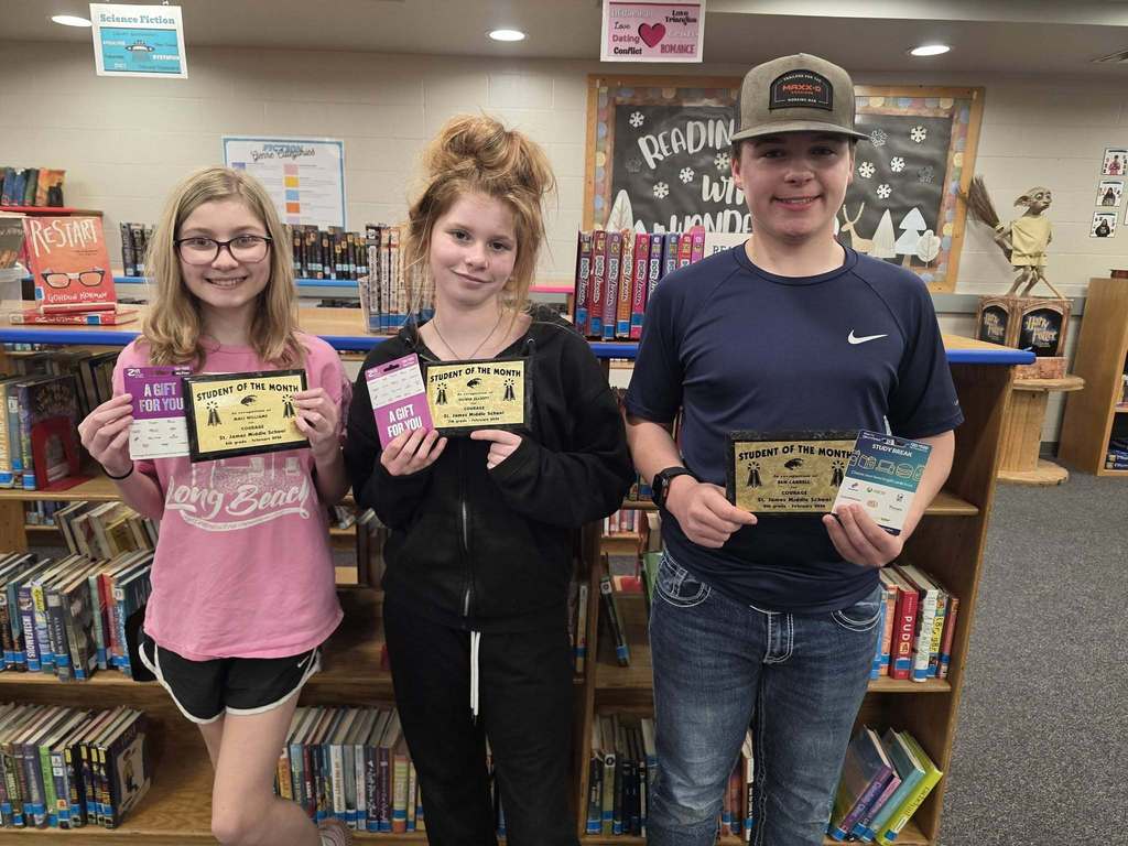 Three people in a library, each holding a certificate. They are smiling and standing next to a bookshelf.
