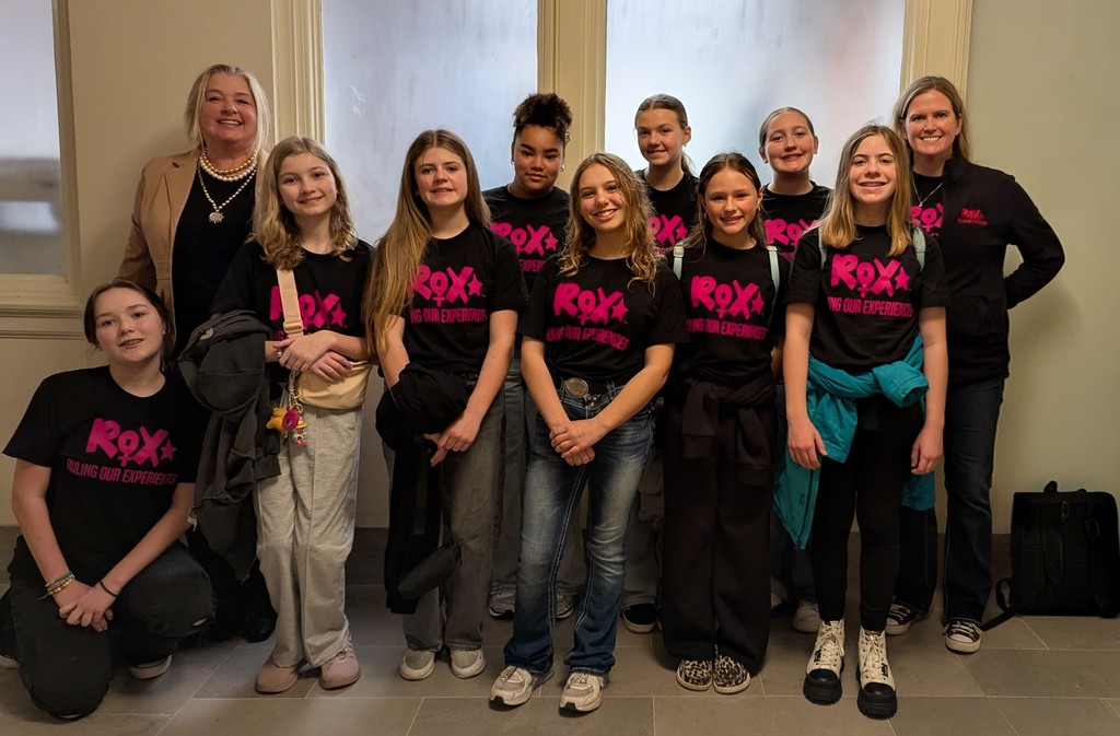 A group of people in black shirts with pink text and numbers pose for a photo.