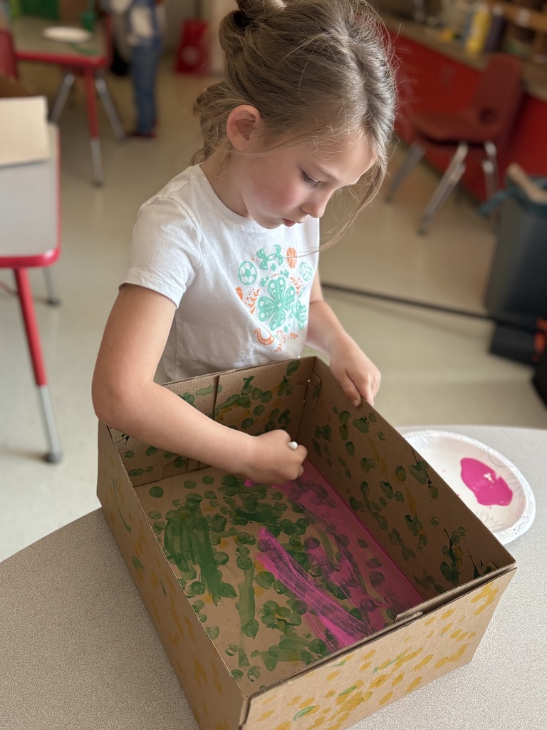 A child examines a cardboard box with painted surfaces, one side pink, the other green.