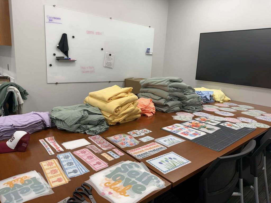 A room with a whiteboard, blackboard, and a table. The table has folded clothes, various cards, and papers.