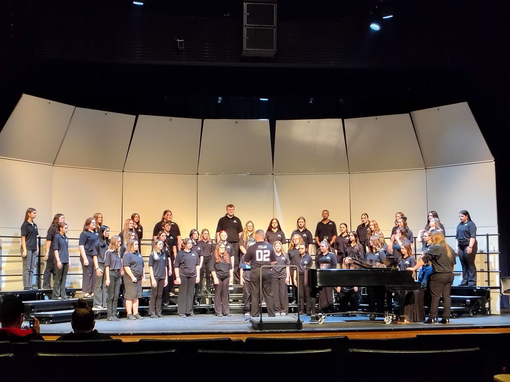 A group of people in matching blue shirts stands on a stage, with some seated and others standing, facing the audience.