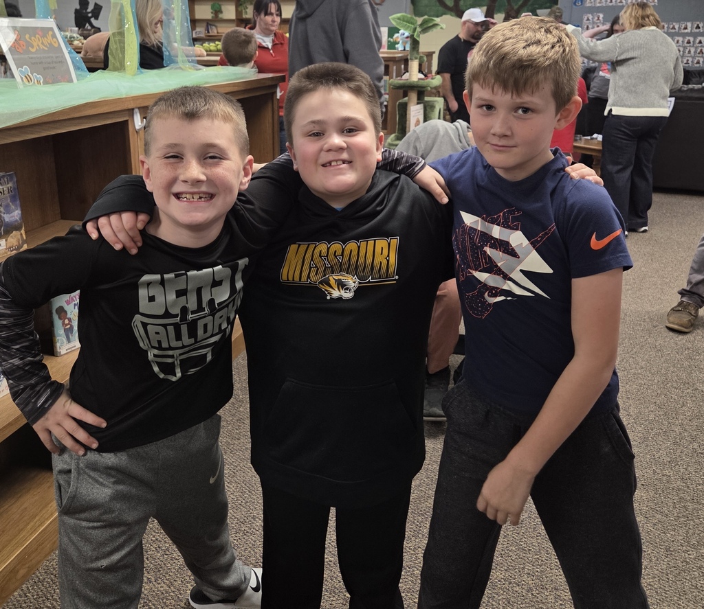 Three boys pose for a picture in a library. One wears a Missouri shirt, another a black shirt, and the third has his hands on the shoulders of the two in front.