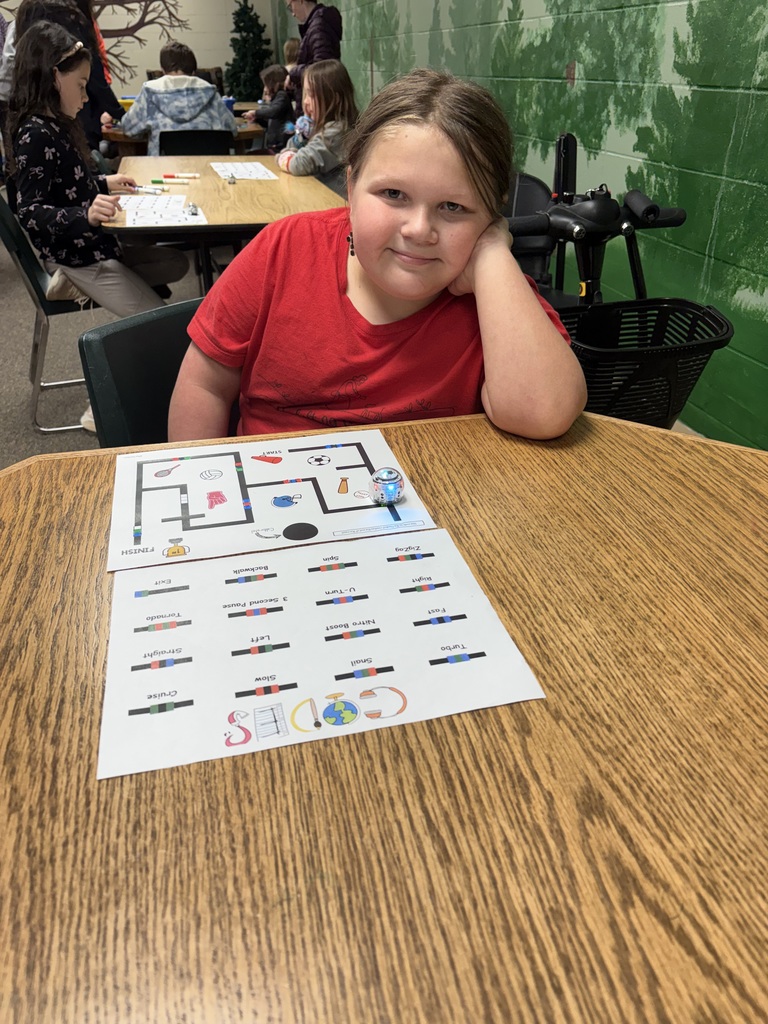 A girl in a red shirt sits at a table with a printed floor plan, smiling.