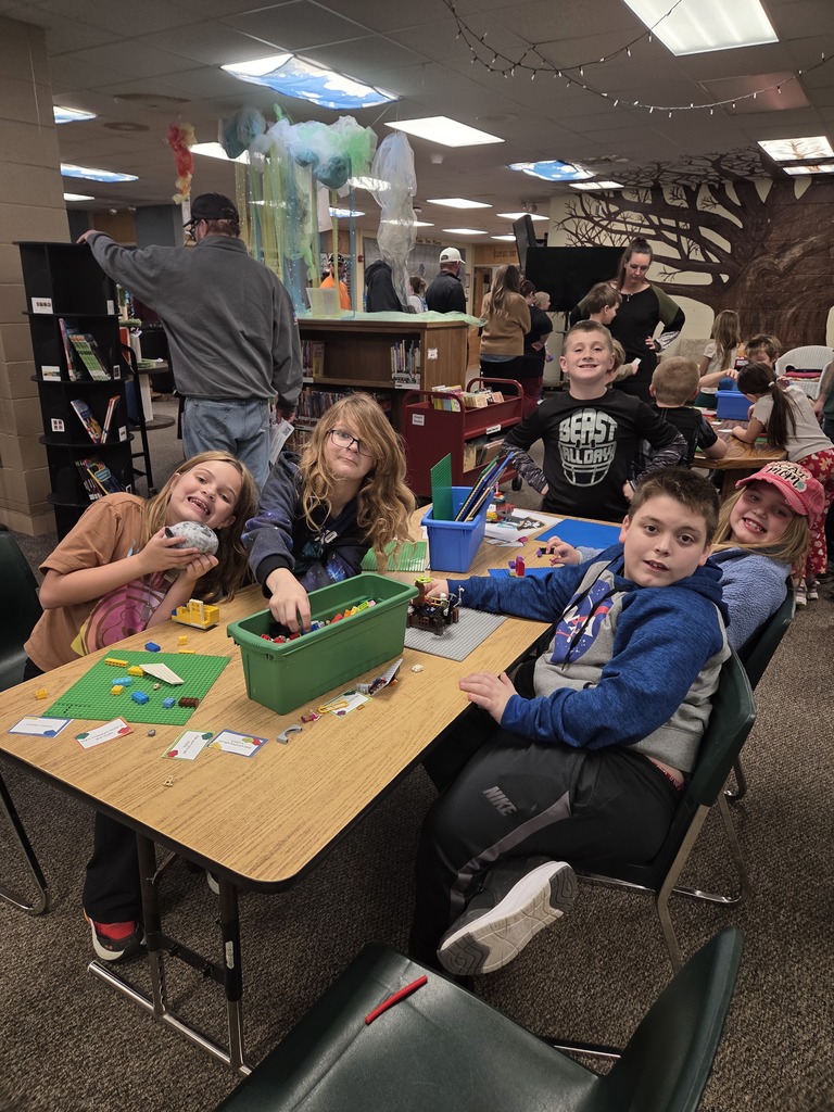 Group of children at a table in a library, sitting on chairs, engaged in an activity with blocks.
