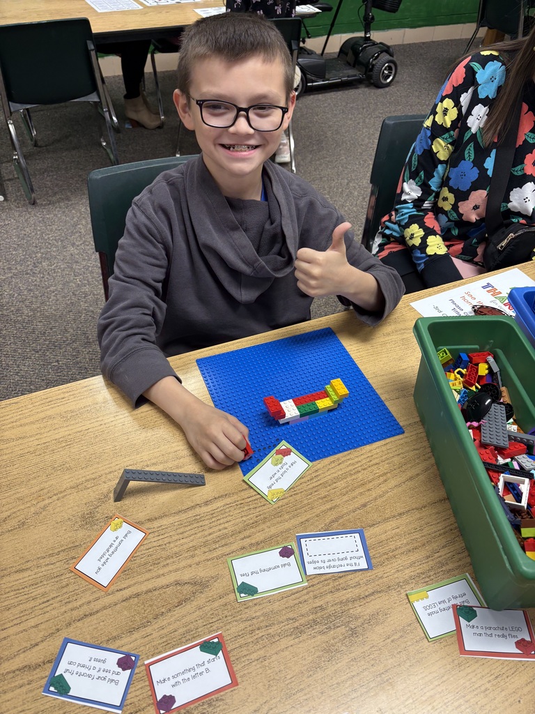 A child wearing glasses sits at a table, smiling, with building blocks and cards on the table.