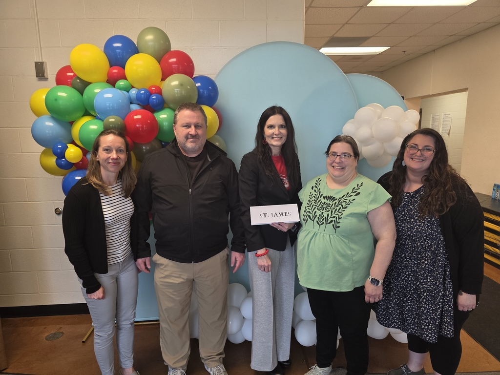 Five adults stand next to each other in front of a large blue cloud with balloons.