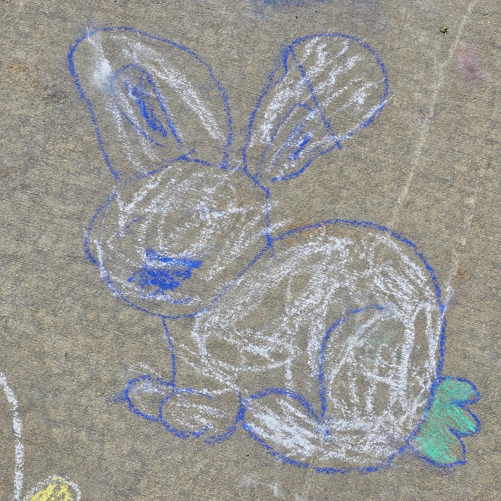 Chalk drawing of a rabbit on a paved surface, with blue outlines and green ears, sitting on gray concrete.