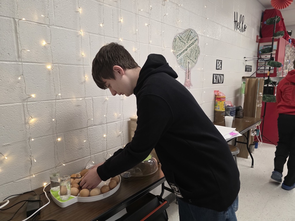 A person in a black hoodie prepares food on a table. A plate with eggs is nearby.