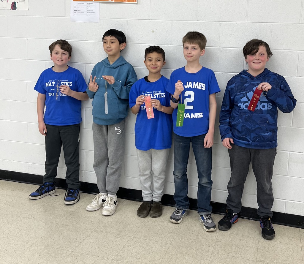 Five boys, all wearing blue shirts, stand against a white wall holding awards. They all have sneakers on.