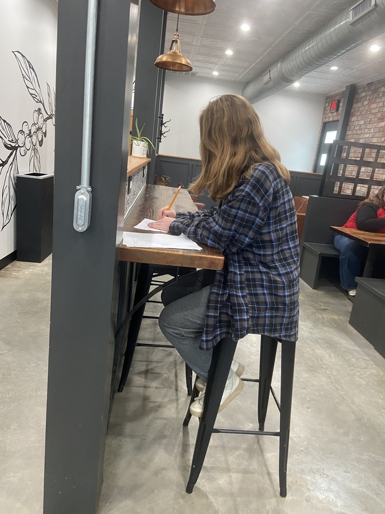 Person in a plaid shirt sitting at a table with papers and a pen, in a booth.