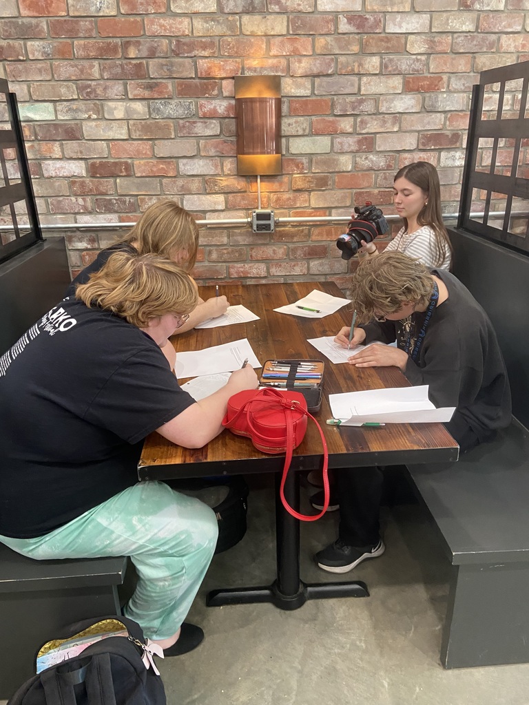 Four people are seated around a table in a room with brick walls, each writing on paper.