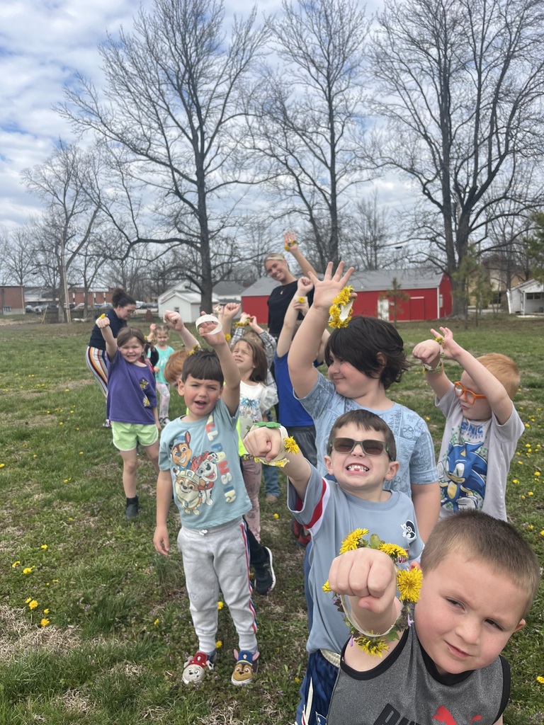 Group of children in outdoor field with bare trees, some wearing yellow bracelets, waving and smiling.