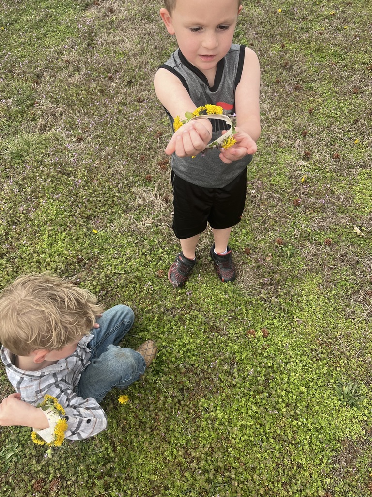 Boy in gray shirt is showing a flower bracelet. 
