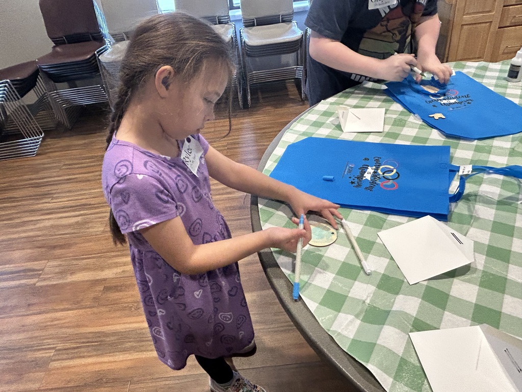 Girl in a purple dress colors standing at a table. 