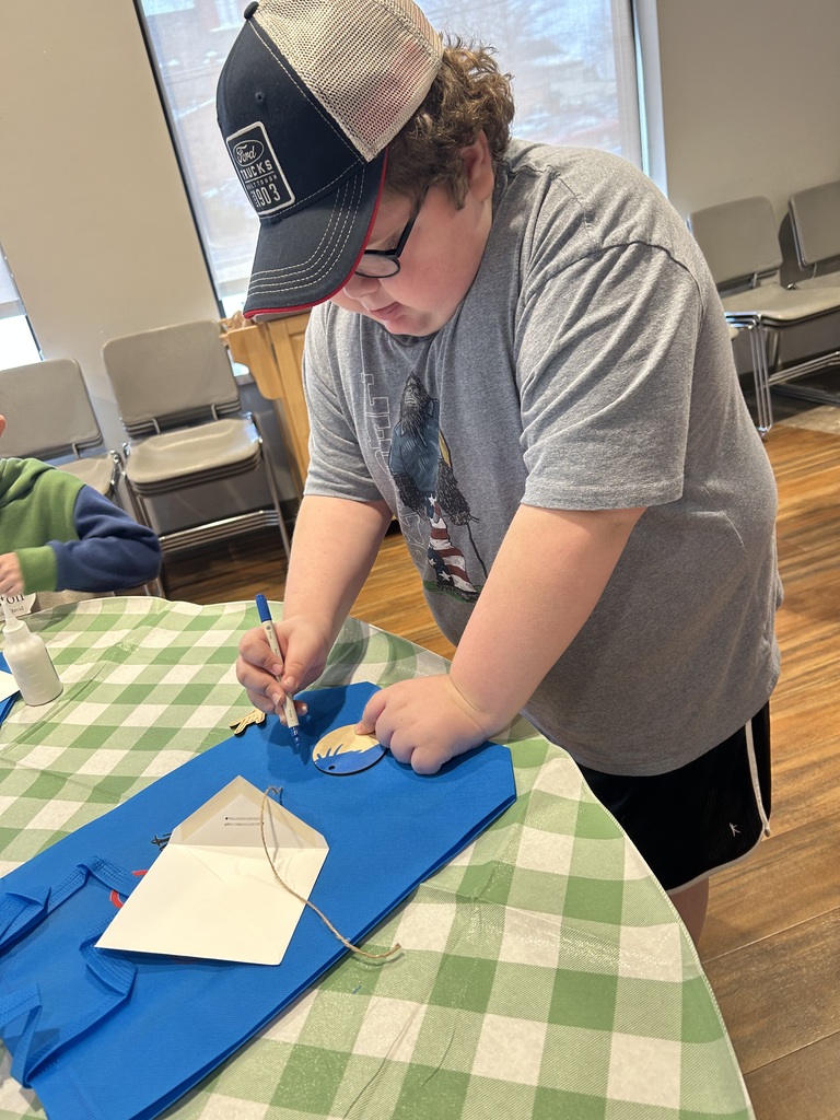 Boy is baseball hat and gray shirt colors whole standing at a table. 